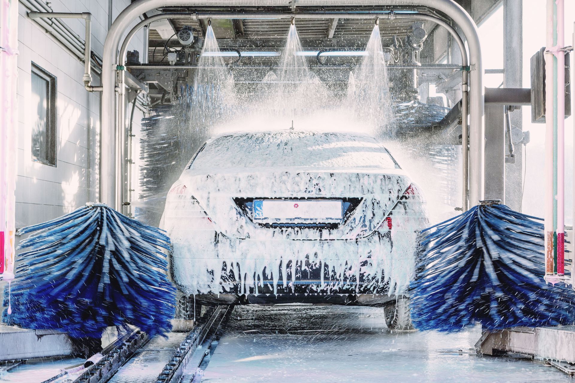 Car in a car wash, covered in soap and being sprayed with water; blue brushes on sides.