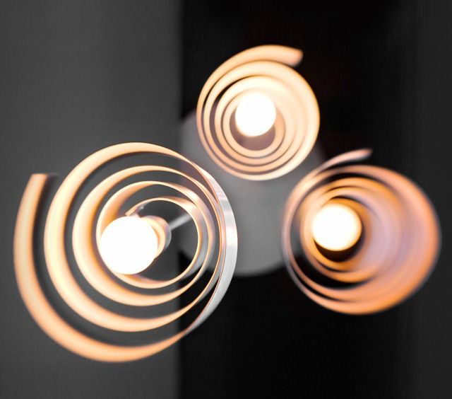 Three spiral-shaped white pendant lights, each with a bright bulb, against a dark background.