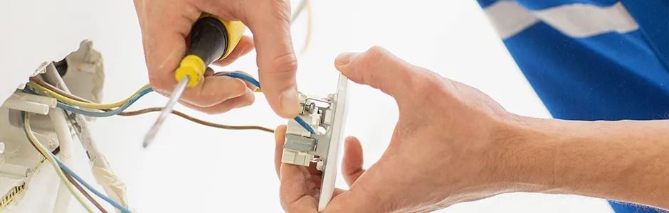 Electrician's hands working on a wall outlet, using a screwdriver to attach wires.
