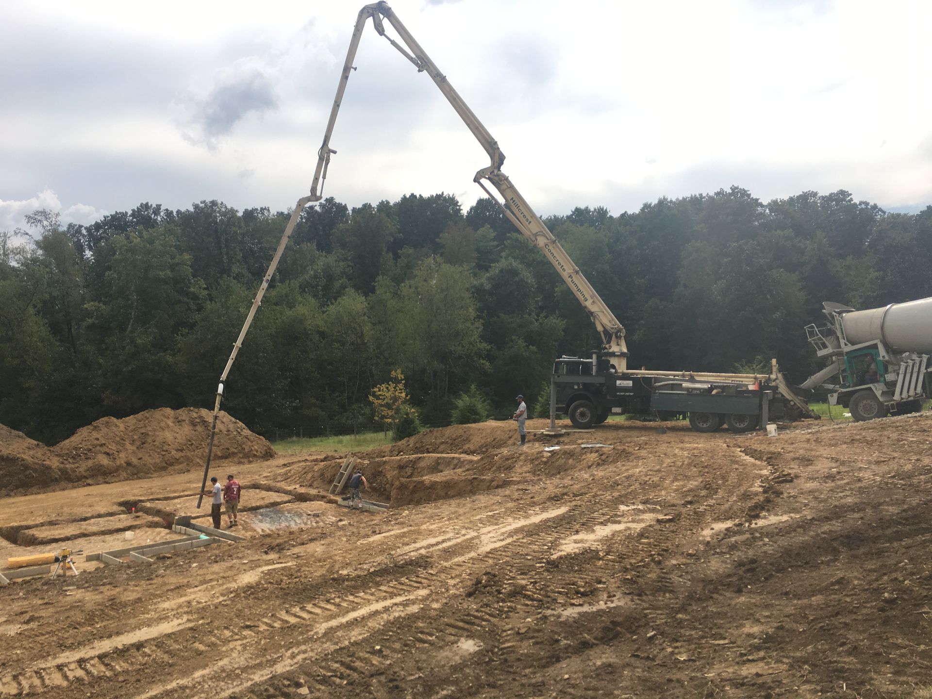 A concrete pump truck pouring cement into a foundation, workers nearby. Construction site.
