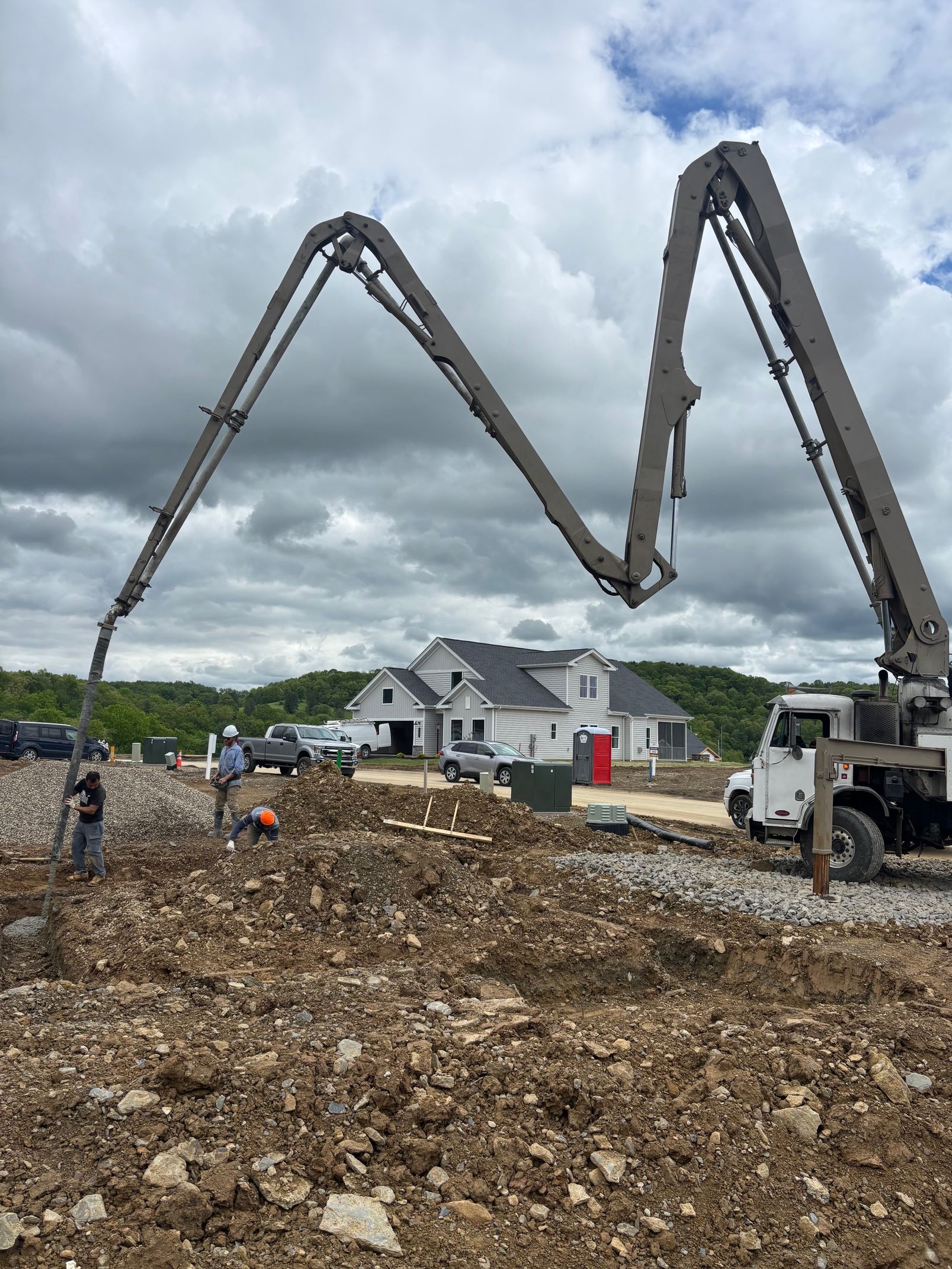 Concrete pump pouring foundation for a new house under cloudy skies. Workers are on-site.