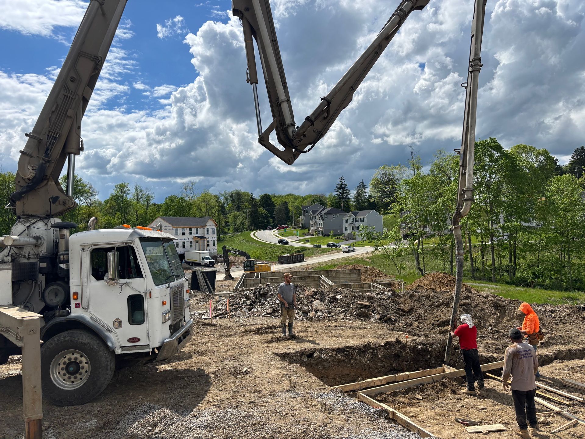 Concrete pump truck pouring concrete at a construction site with workers. Sunny day with houses in the background.