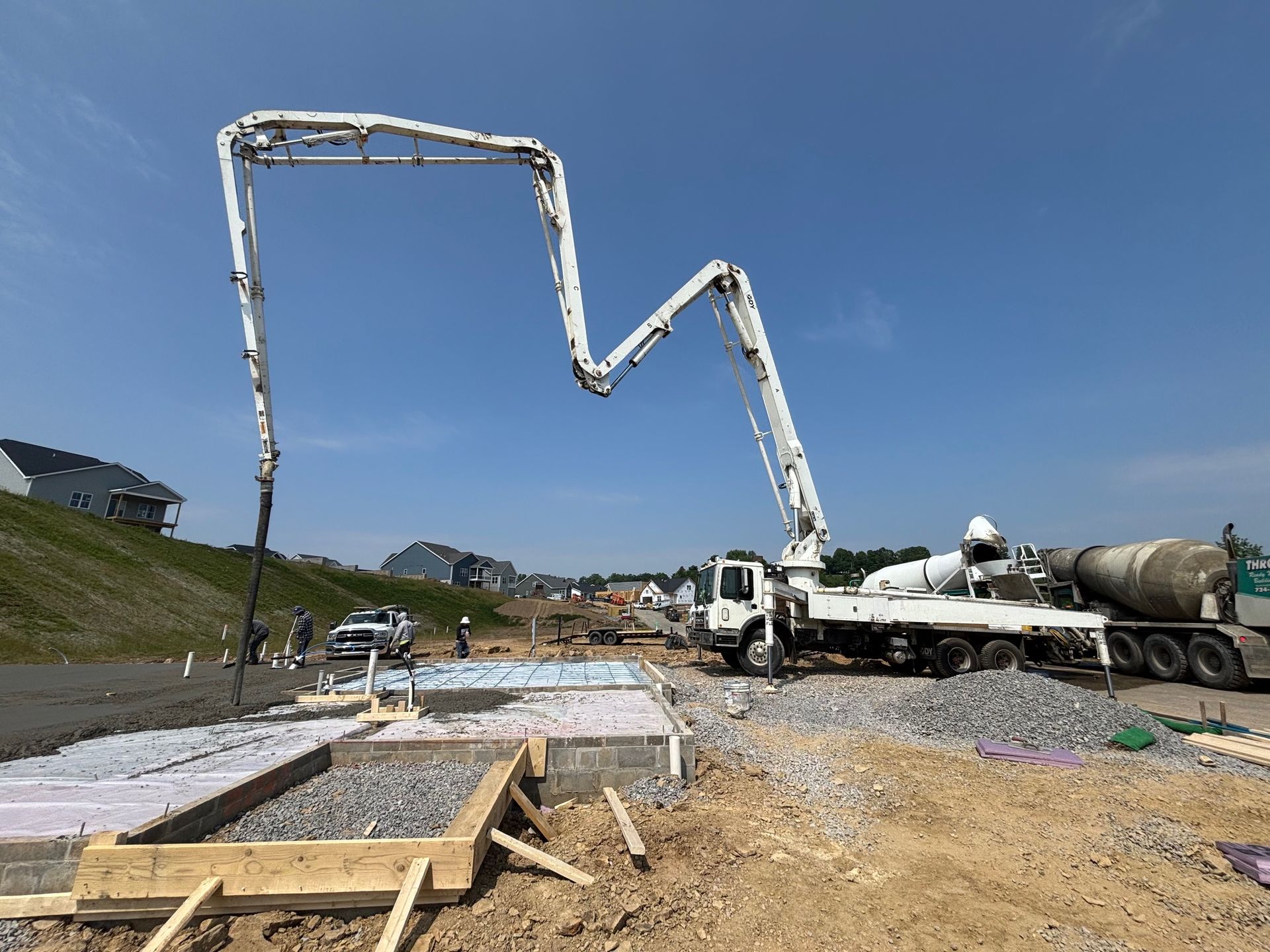 Concrete pump truck pouring concrete into a foundation form on a construction site. Blue sky.