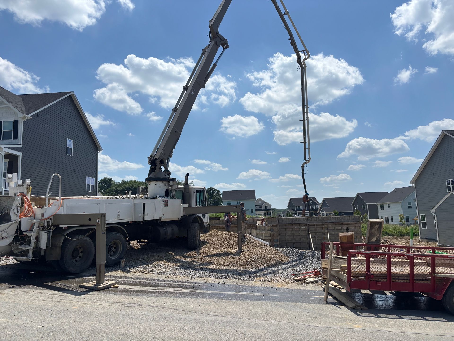 Concrete pump truck pouring concrete into a construction site with houses in the background.