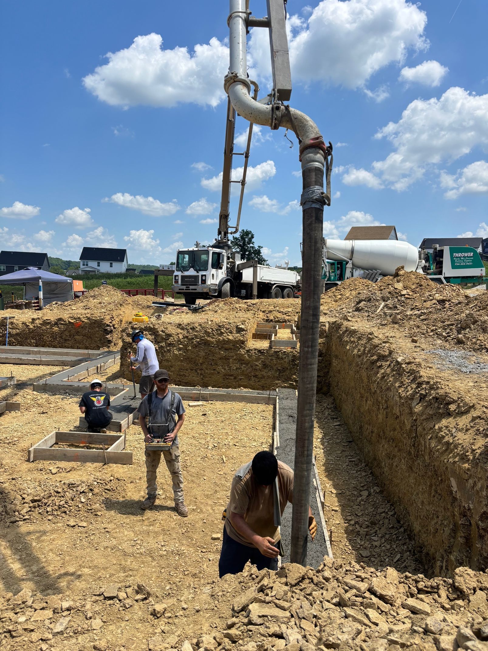Construction workers pouring concrete into a foundation trench with a pump truck under a blue sky.