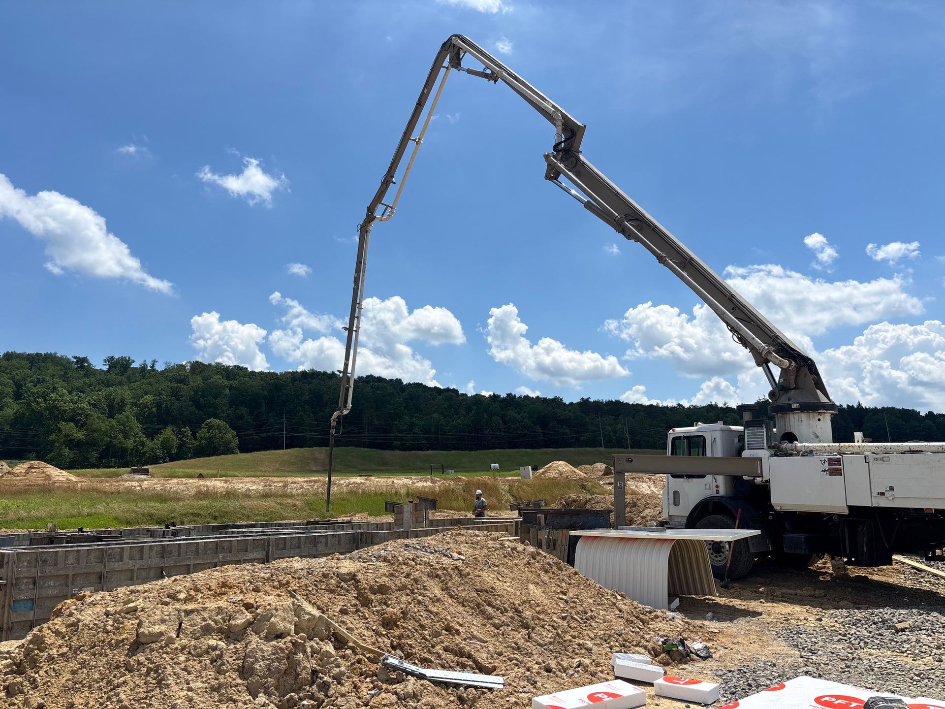 Concrete pump truck pouring concrete into a construction foundation on a sunny day.