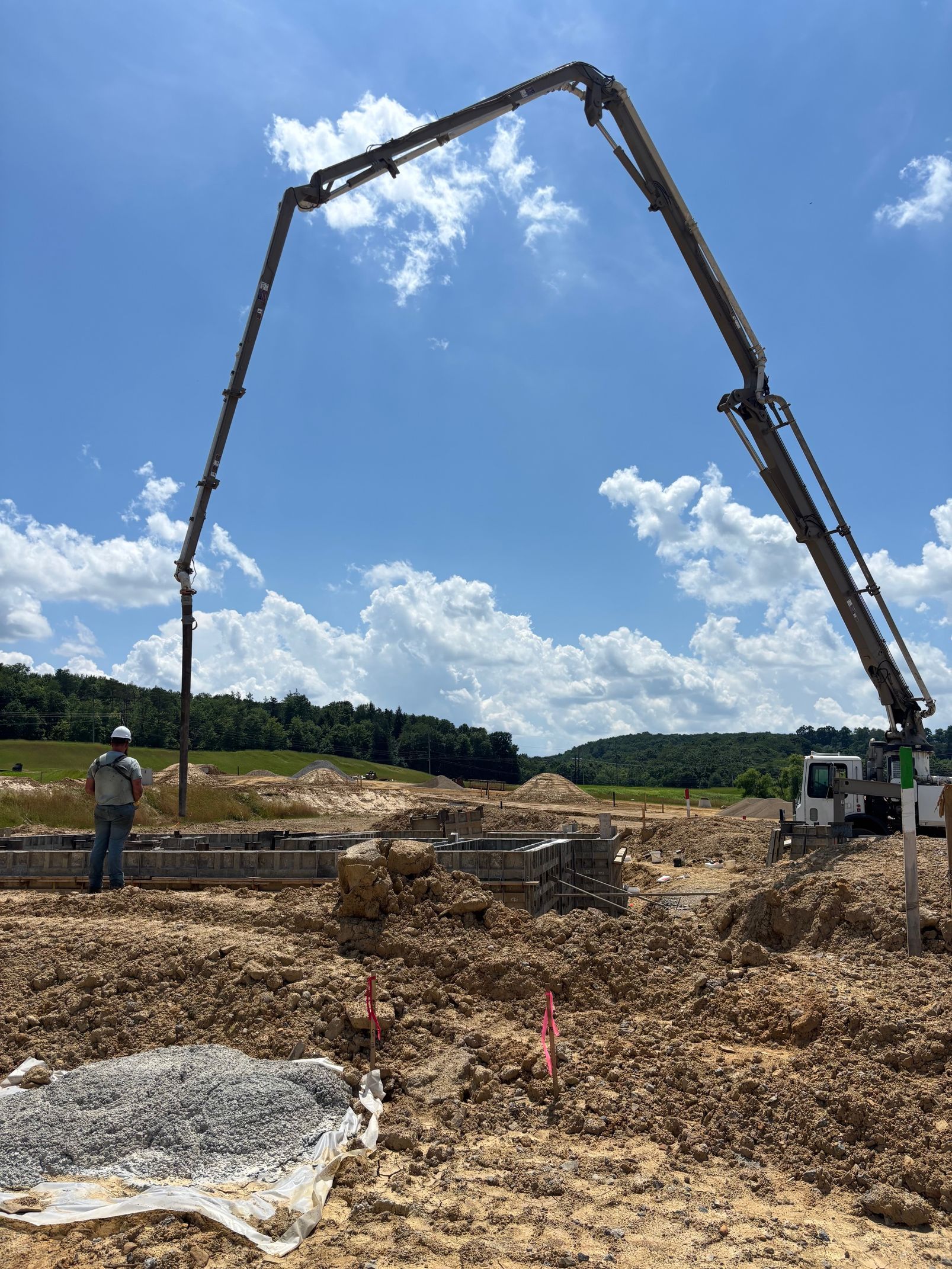 Concrete pump truck pouring concrete into a construction site foundation on a sunny day.