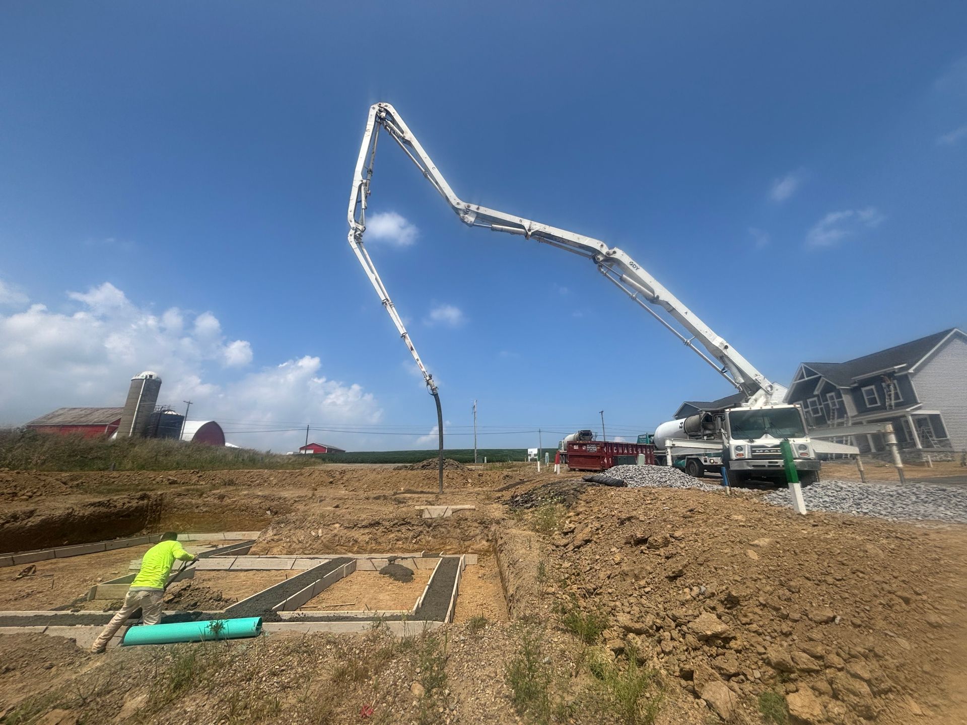 Construction site: concrete pump truck pouring concrete into foundation. Man working on drainage pipes.
