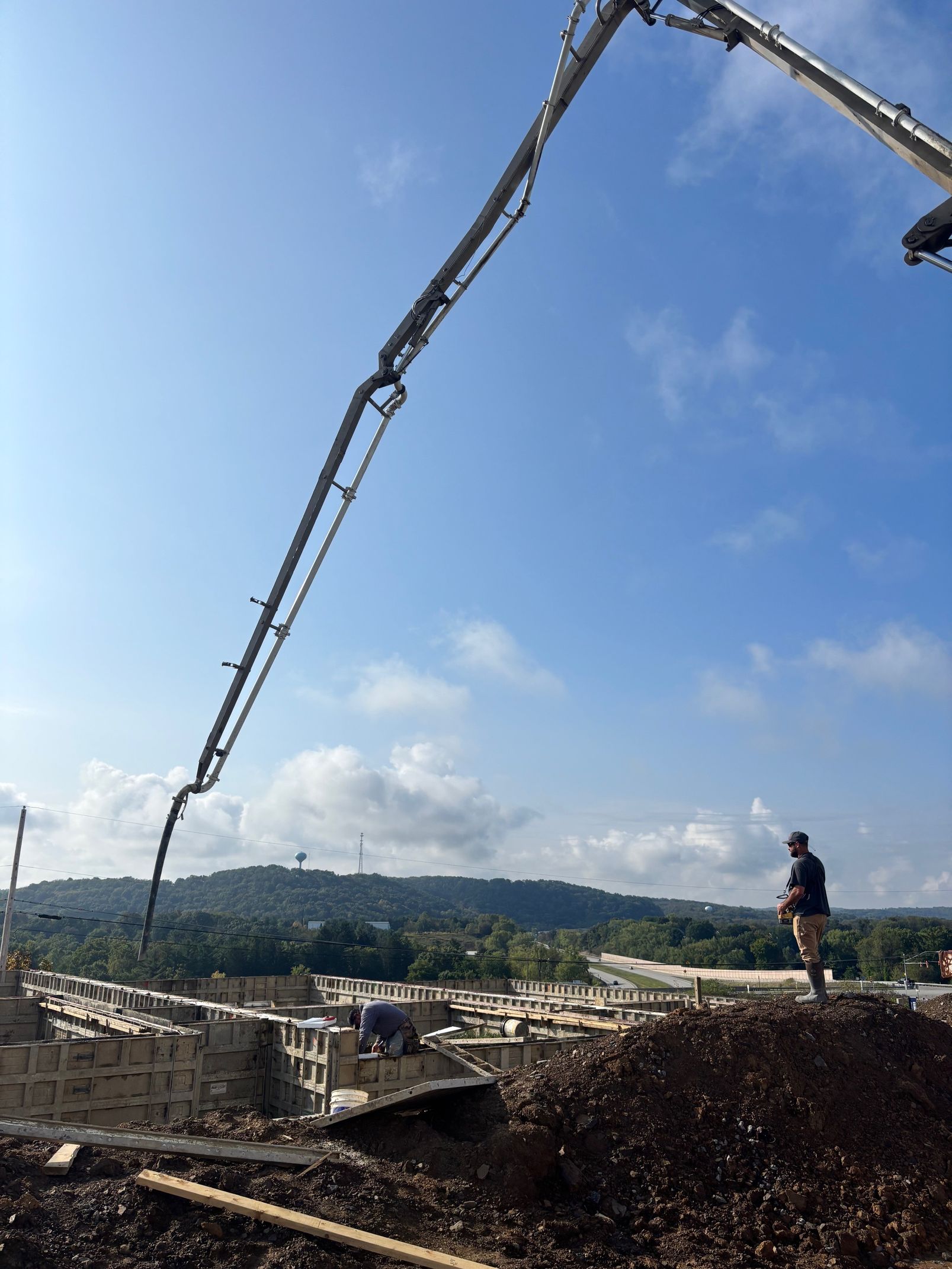 Concrete pump pouring concrete on a building under construction, person standing nearby, bright blue sky in background.