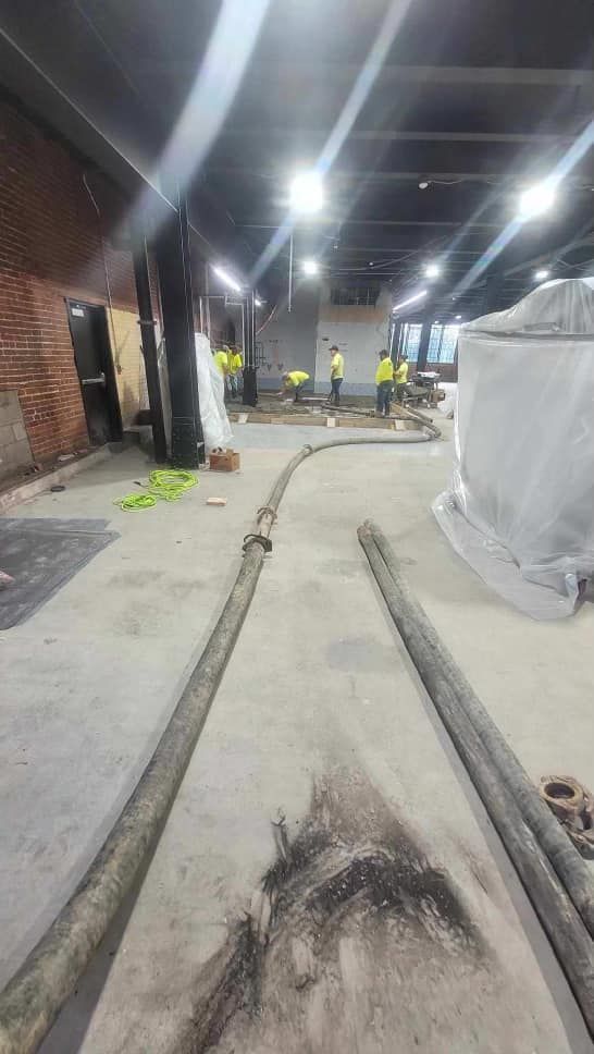 Concrete pour in a construction site; workers in vests, hoses on floor.