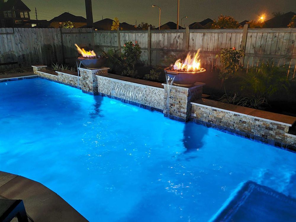 A swimming pool with a fire pit in the middle of it at night.