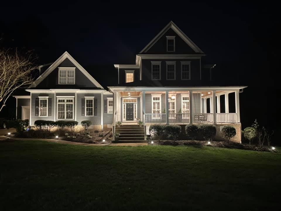 Nighttime view of a lit gray Victorian house with a porch and dark lawn