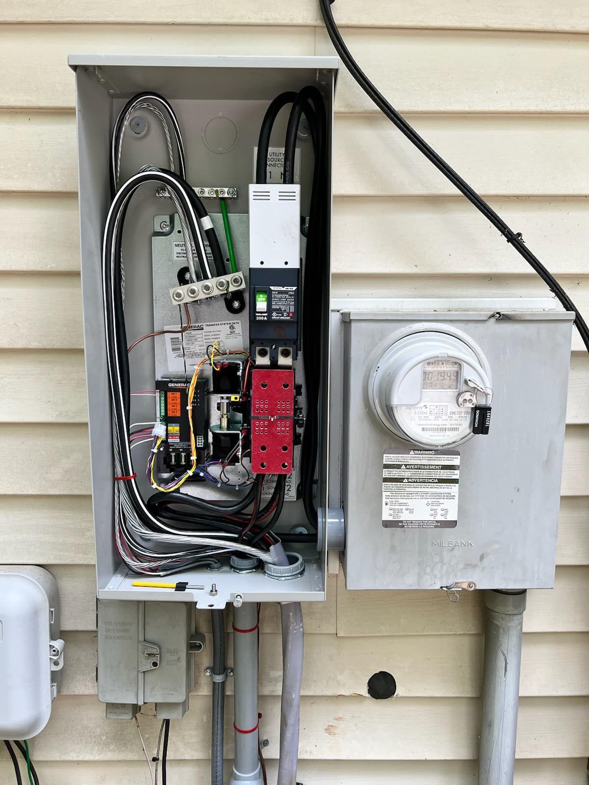 Open electrical meter and breaker panel mounted on an exterior wall, with exposed wiring and conduit.