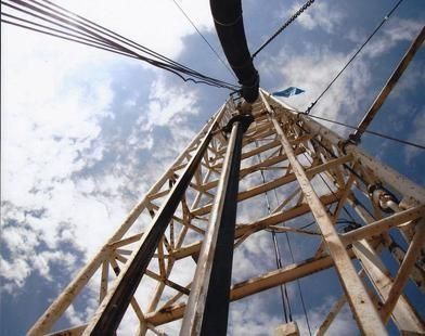 Low-angle view of a metal tower with cables against a cloudy blue sky
