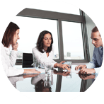Three people in a meeting at a table by a window, discussing papers and looking at a glass.