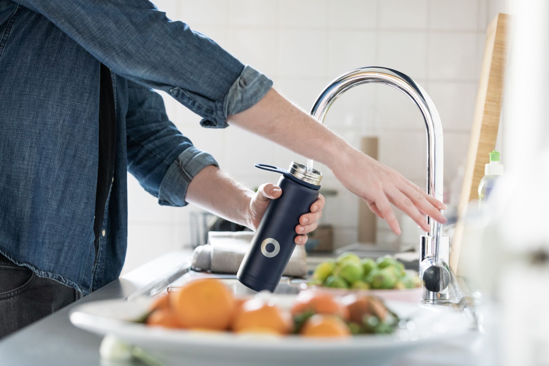 Person filling a dark blue water bottle with water at a kitchen sink.