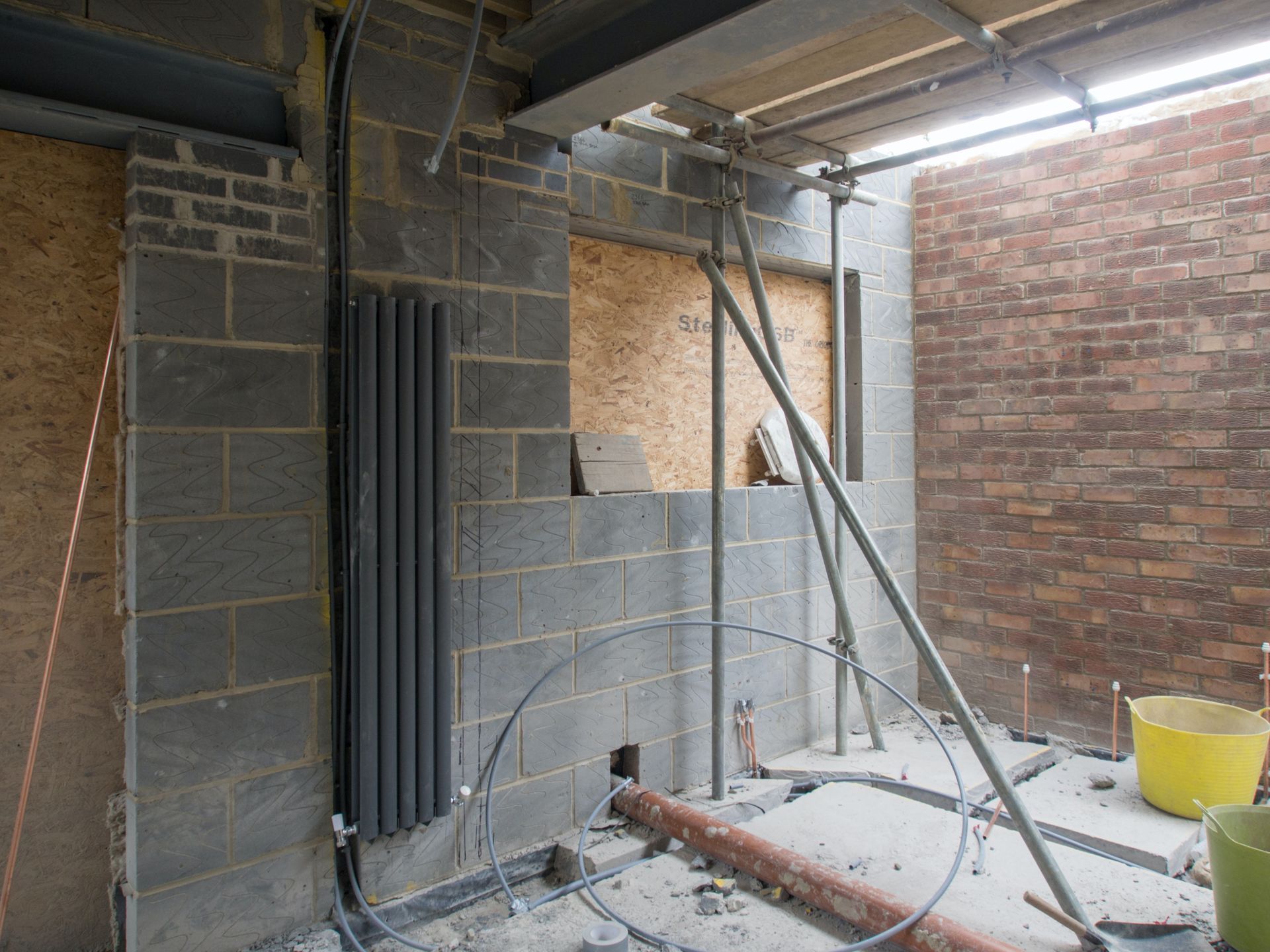 Construction site with exposed block walls, plumbing, scaffolding, and a radiator.