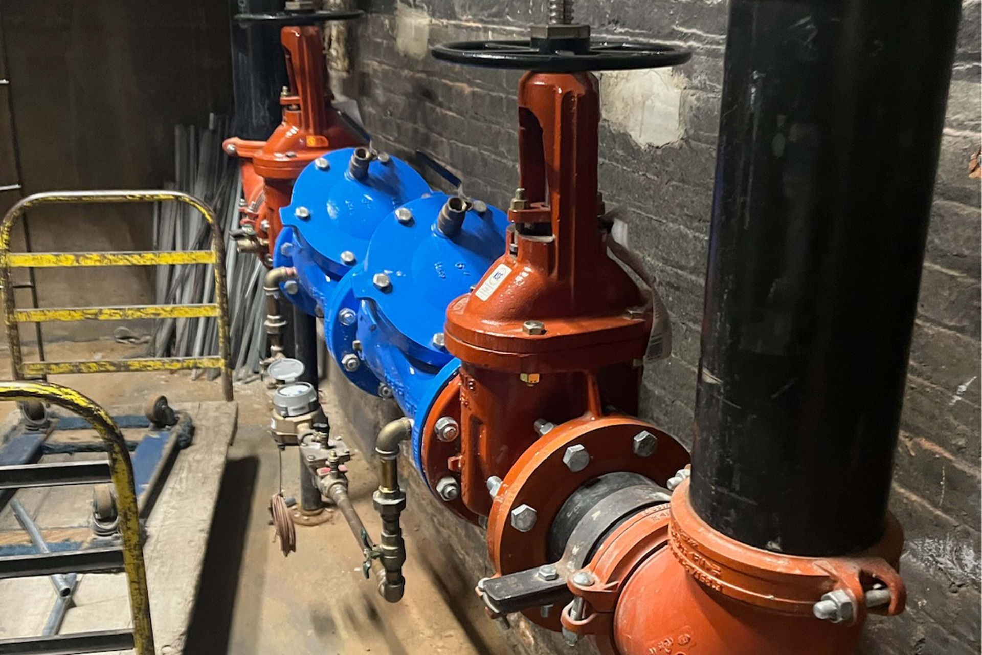 Two large industrial valves, one blue, one red, with black pipes, set in a utility room.