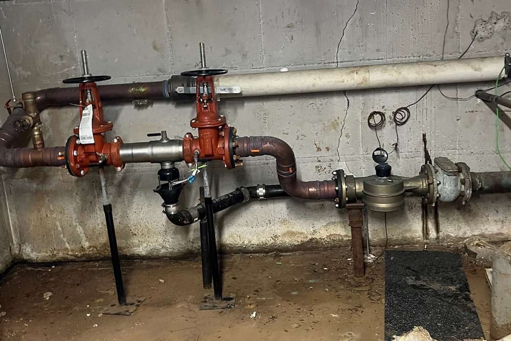 Pipes with red valves and water meter in a basement.
