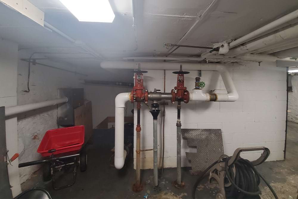 Basement interior with pipes, valves, and a red wheelbarrow.