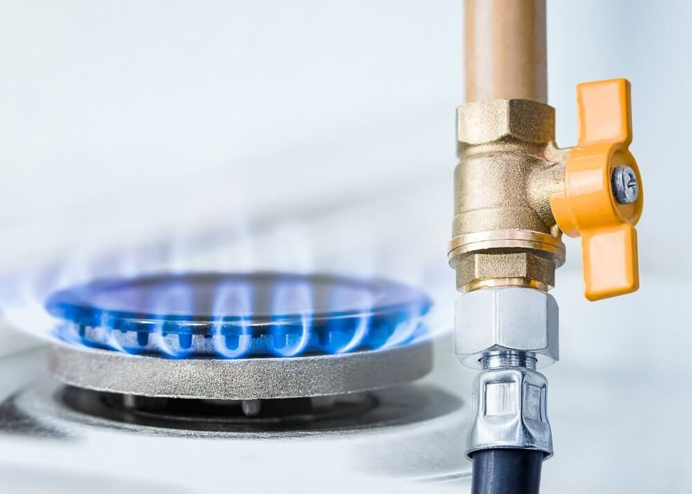Gas stove burner with blue flames, next to a gas valve with an orange handle.