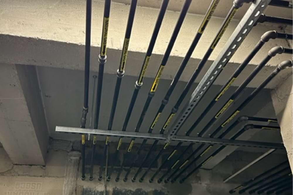 Black pipes with yellow labels and metal supports run across a concrete ceiling.