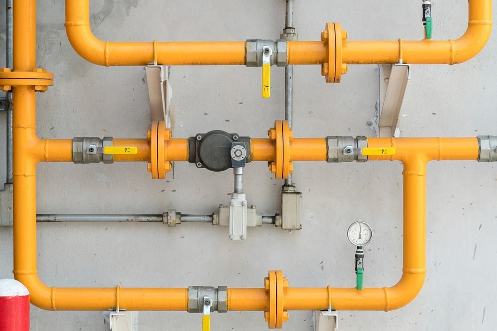 Yellow pipes with valves and gauges against a concrete wall.