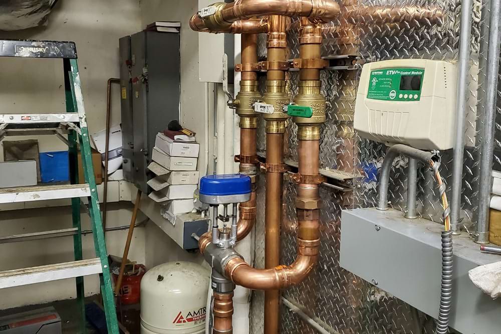 Copper pipes and valves against a diamond plate wall, with control panel and water tank.