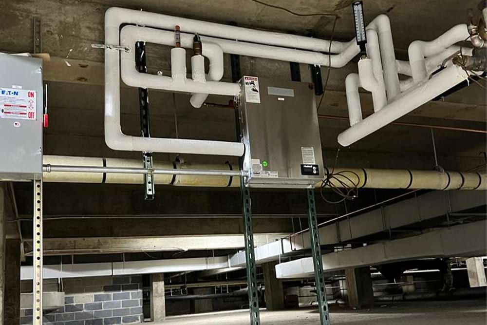 HVAC unit with insulated pipes suspended from a concrete ceiling, likely in a commercial building.