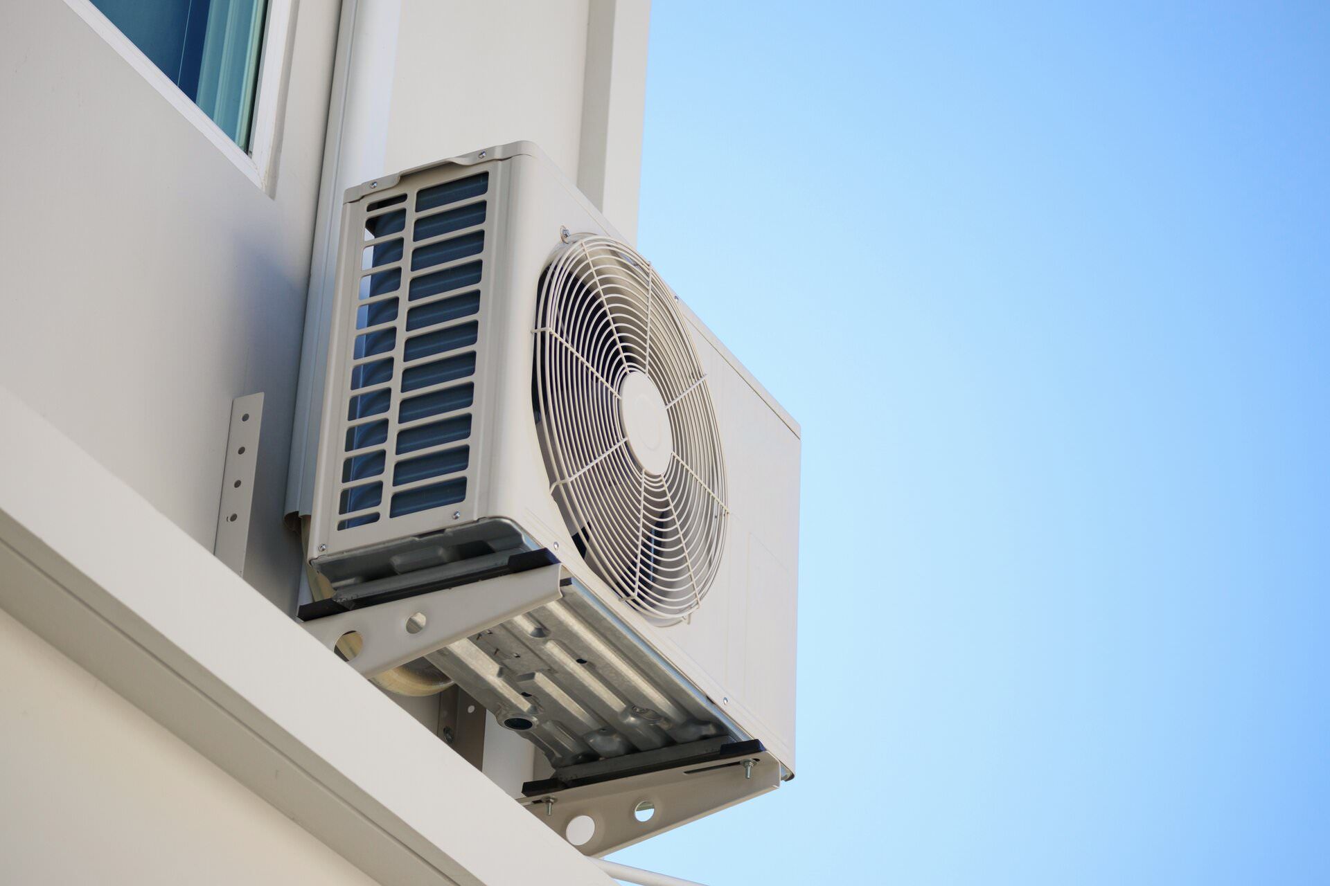 Outdoor air conditioning unit mounted on a white building against a blue sky.