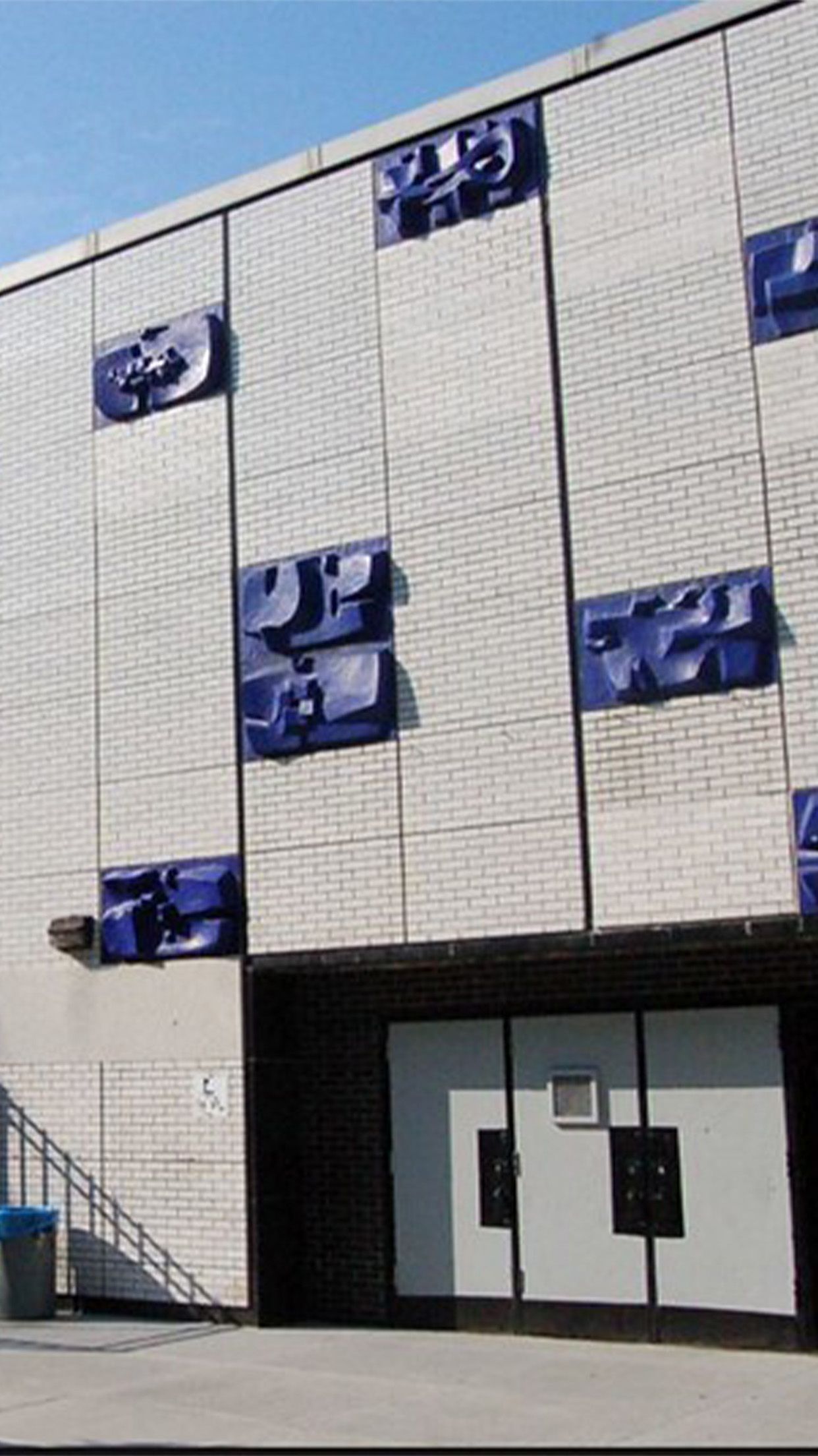 Brick building exterior with blue, abstract relief art. Entrance beneath.