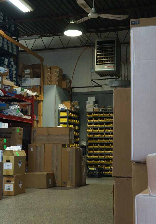 Warehouse interior with boxes, shelving, and parts bins. An overhead heater and fan are visible.