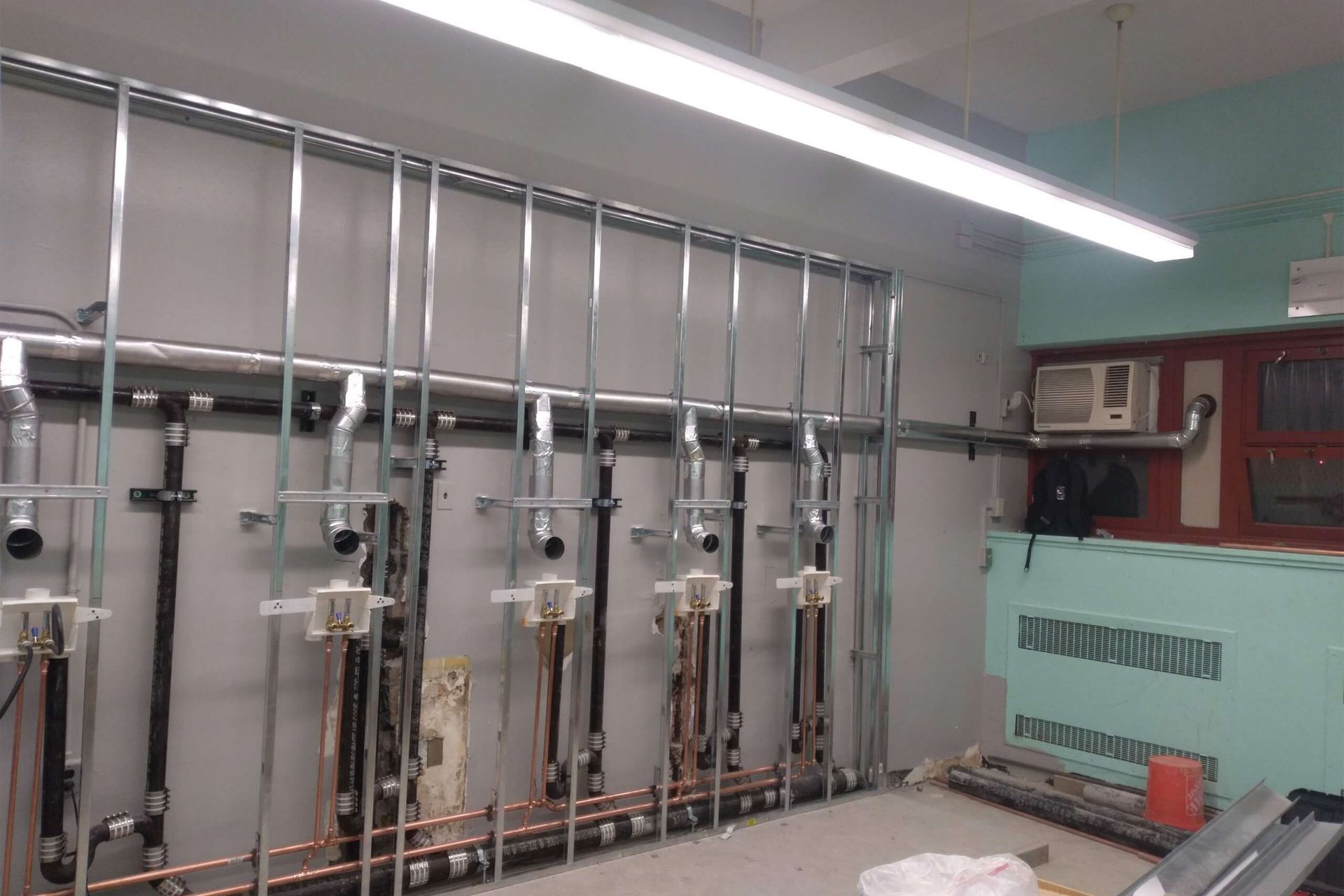 Pipes, metal framing, and other plumbing components along a wall in a building under construction.