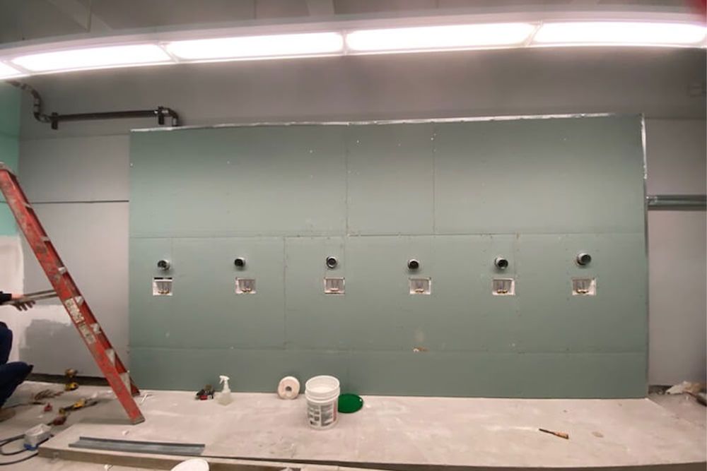 Wall construction with plumbing fixtures installed. A ladder, tools, and materials are nearby.