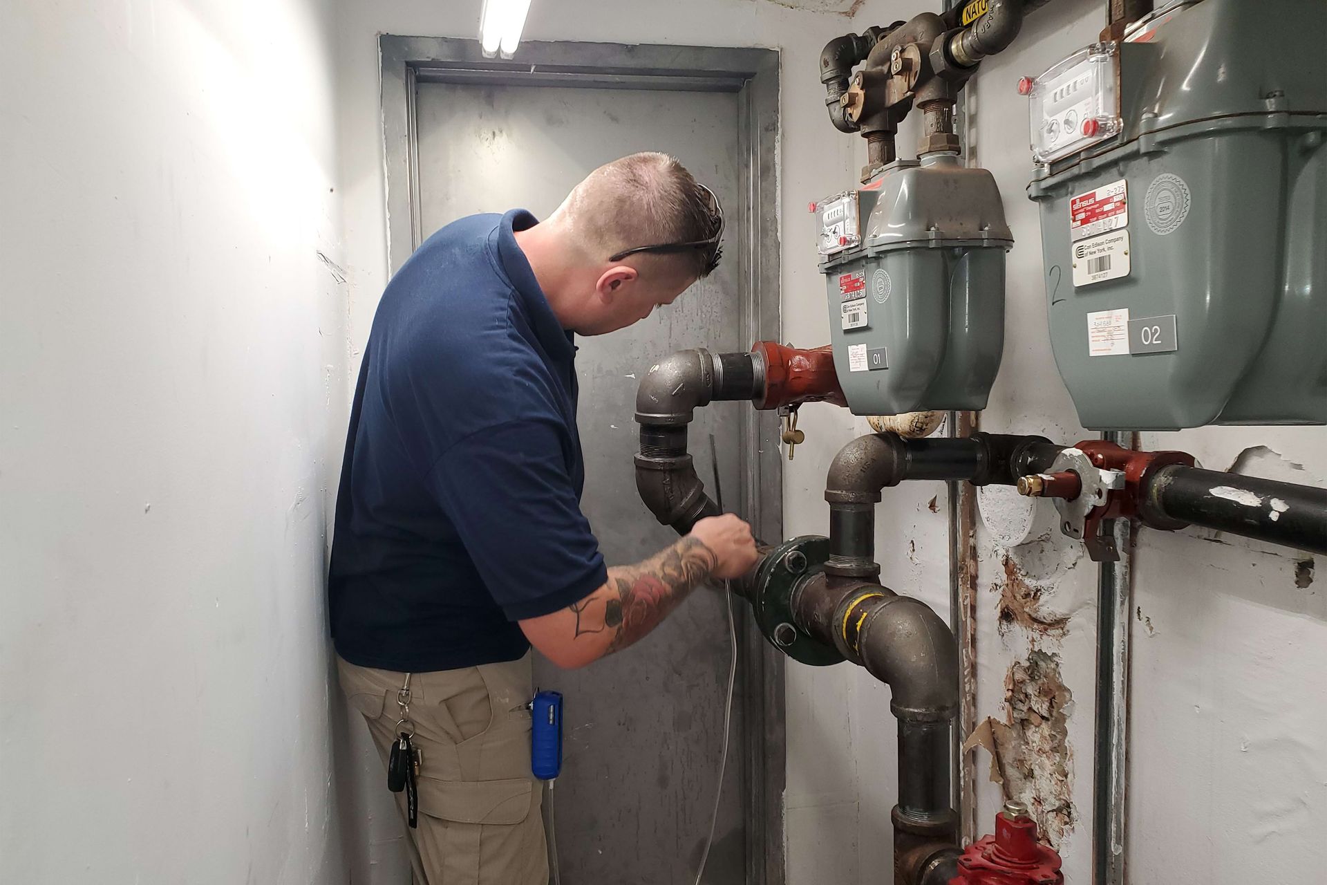 Person in blue shirt working on gas pipes in a utility room.