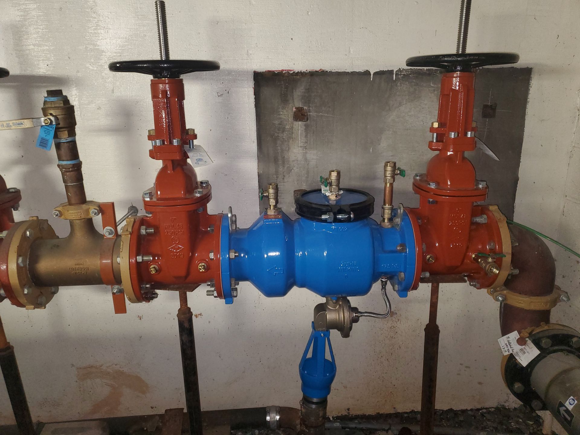 Plumbing system with red and blue valves, black handwheels, connected by metal pipes against a white wall.