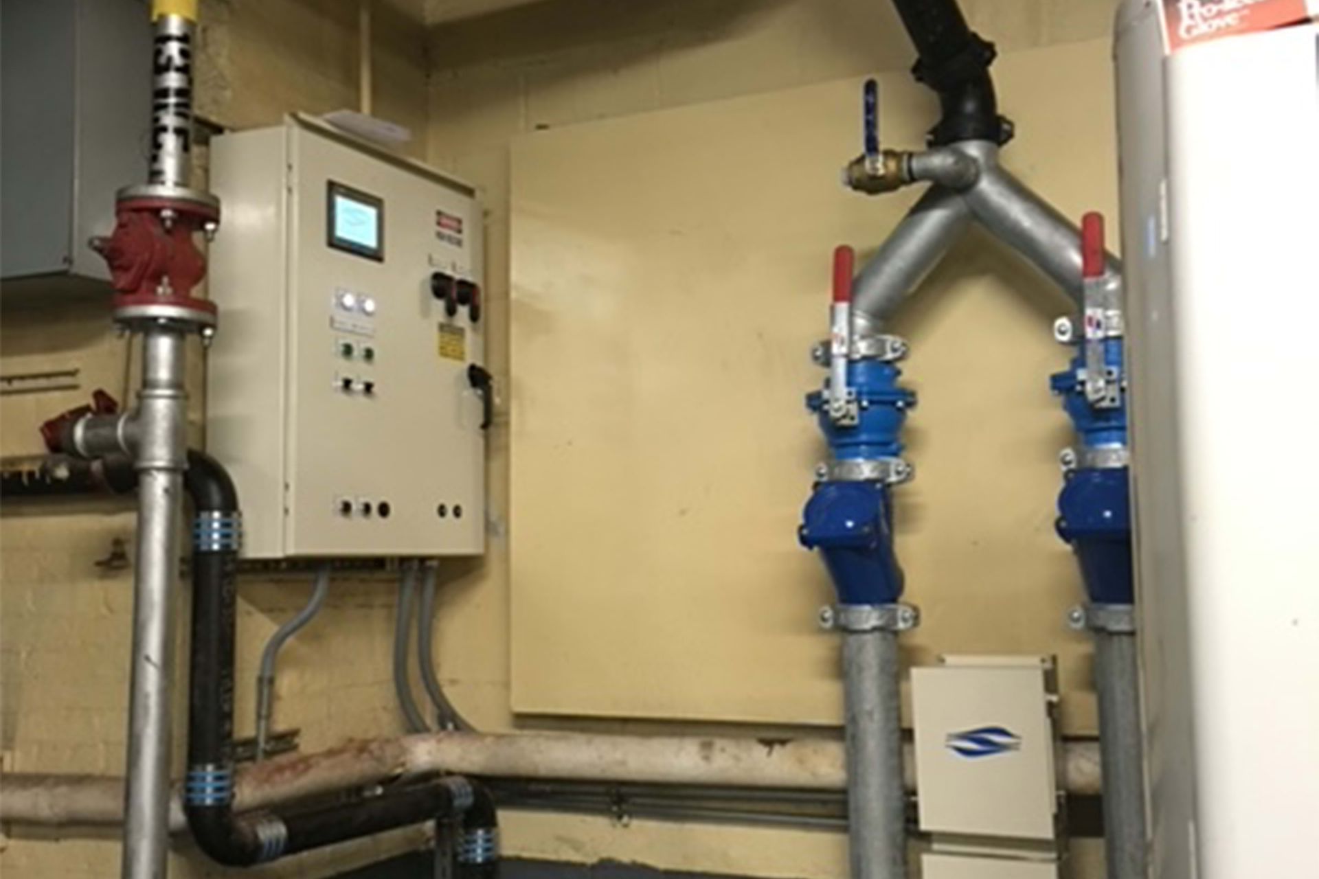 Pipes and valves connected to a control panel in an industrial setting. Some valves are red or blue.
