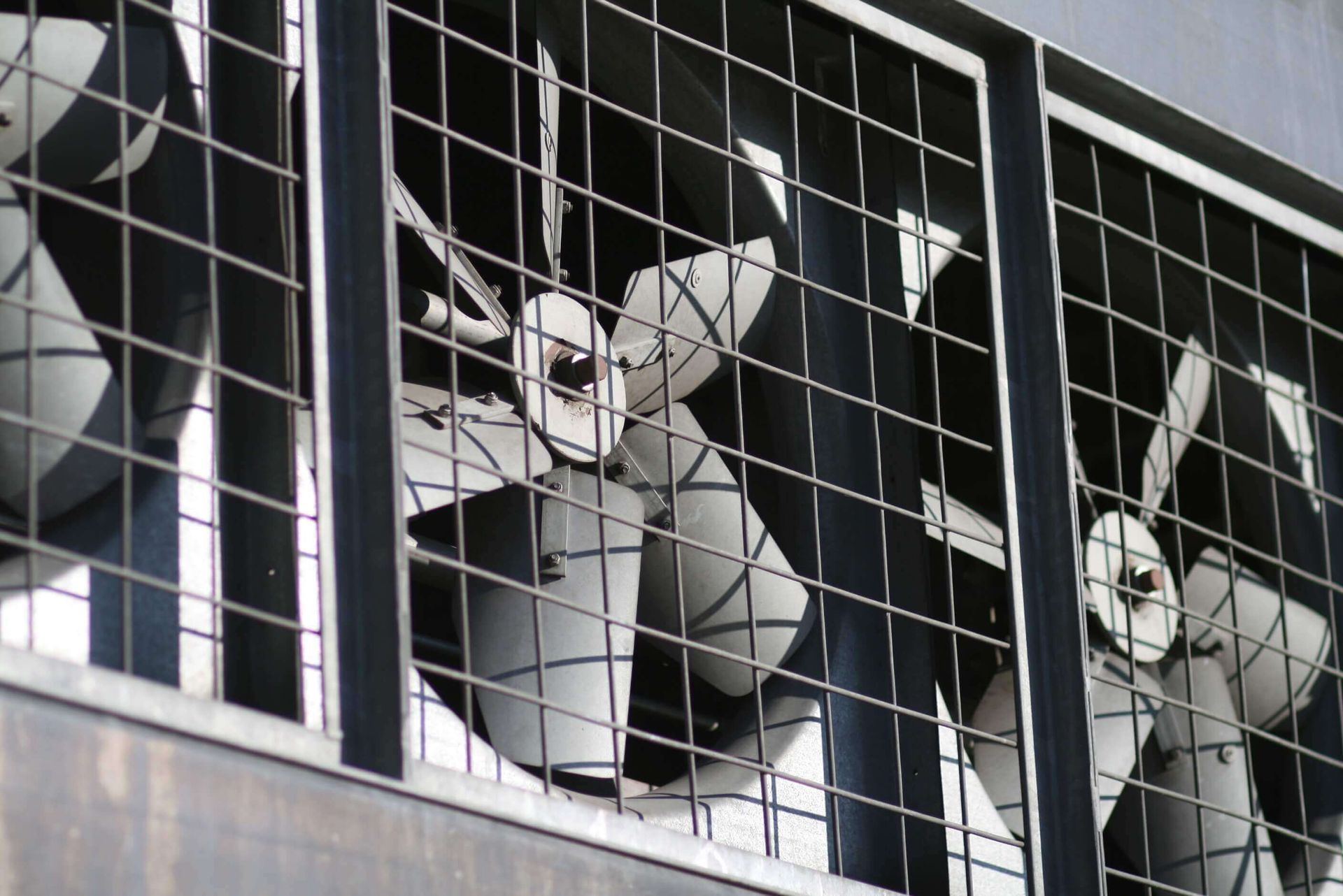 Three industrial fans behind protective metal grates, mounted on a building.