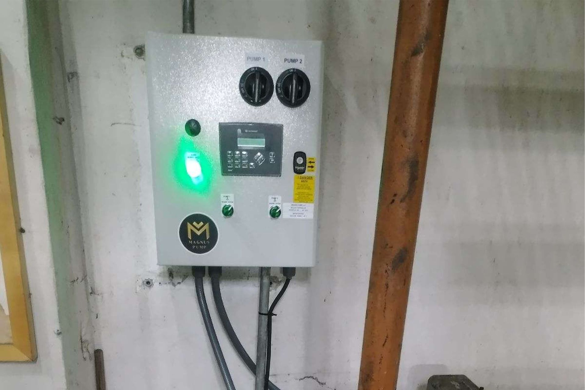 A light-gray electrical control panel on a wall with green indicator lights; brown wooden beam is nearby.