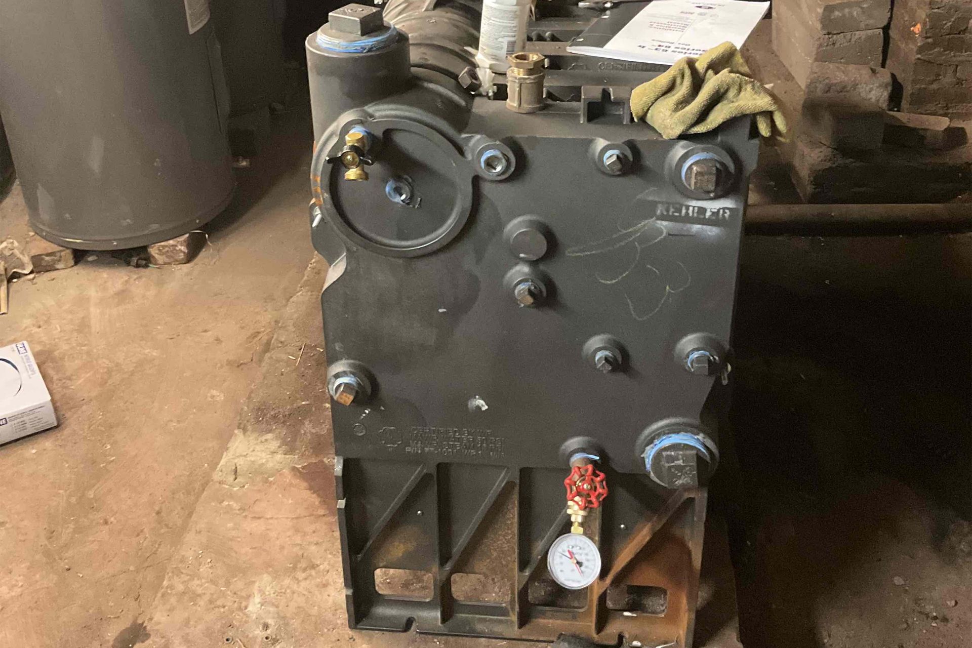 Large, gray industrial machine with multiple bolts and gauges, set in a dimly lit, wooden-floored space.