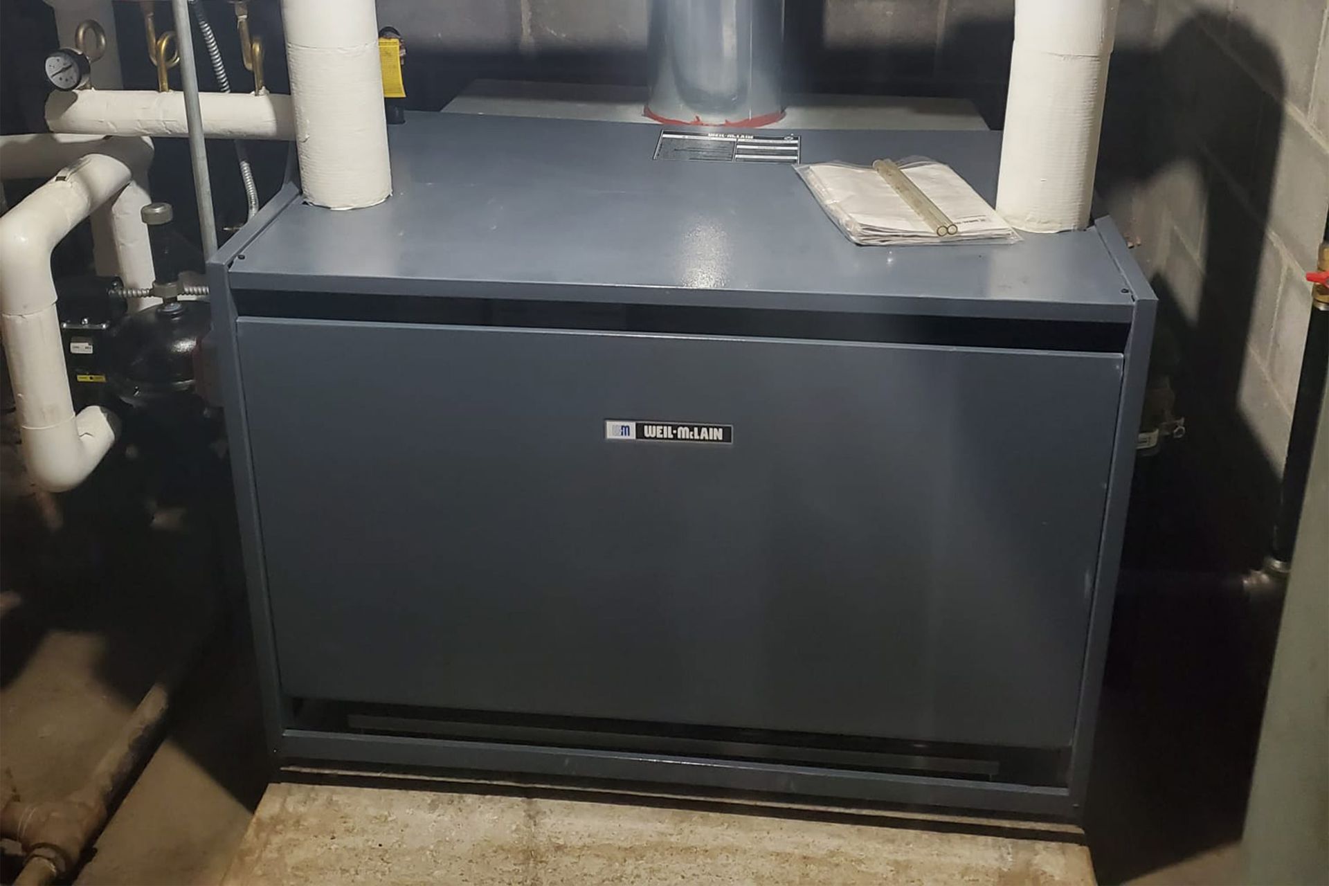 Gray HVAC unit in a basement setting, with white pipes and insulation.
