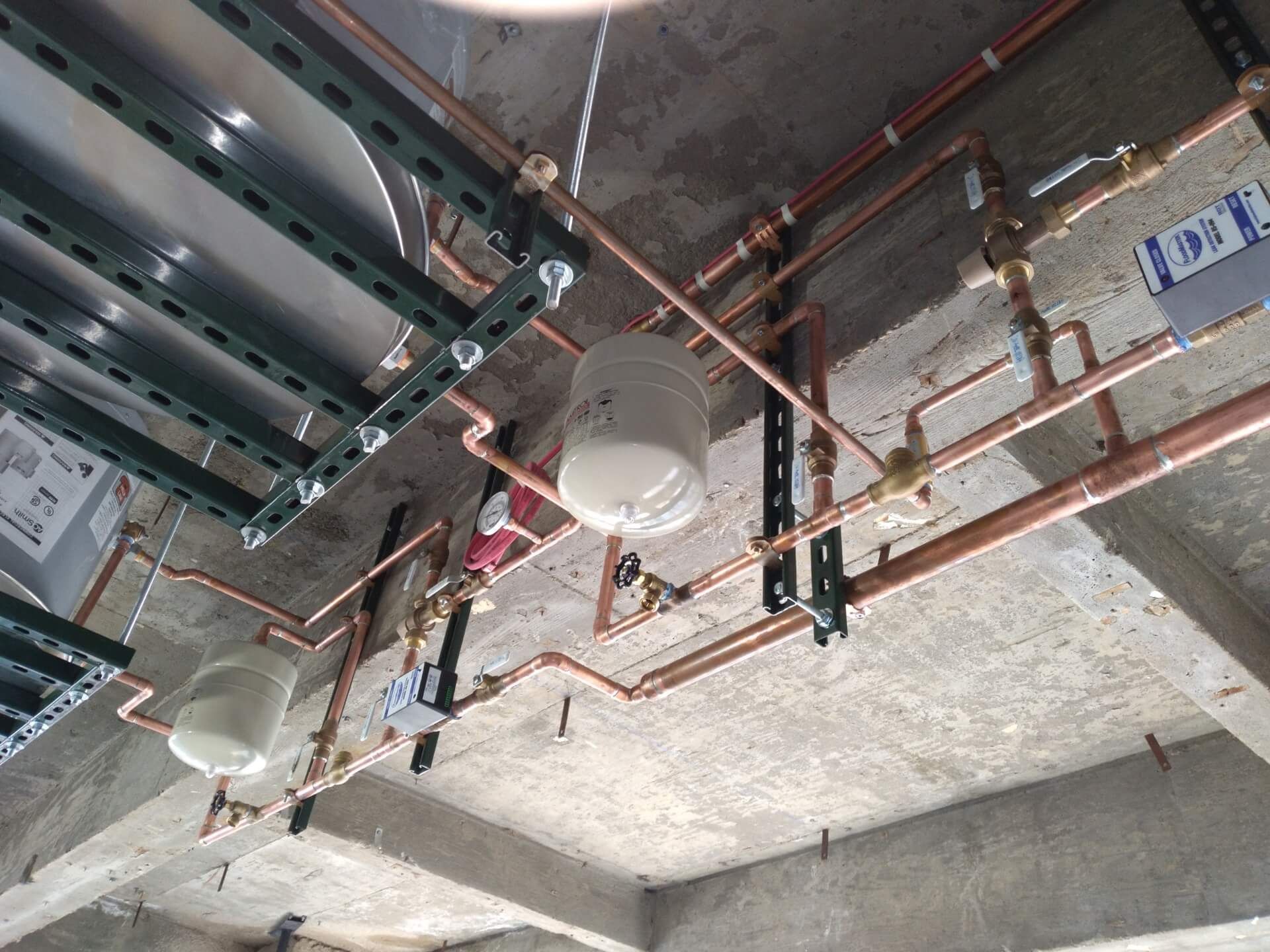 Copper pipes and valves installed on a concrete ceiling, likely for a building's plumbing system.