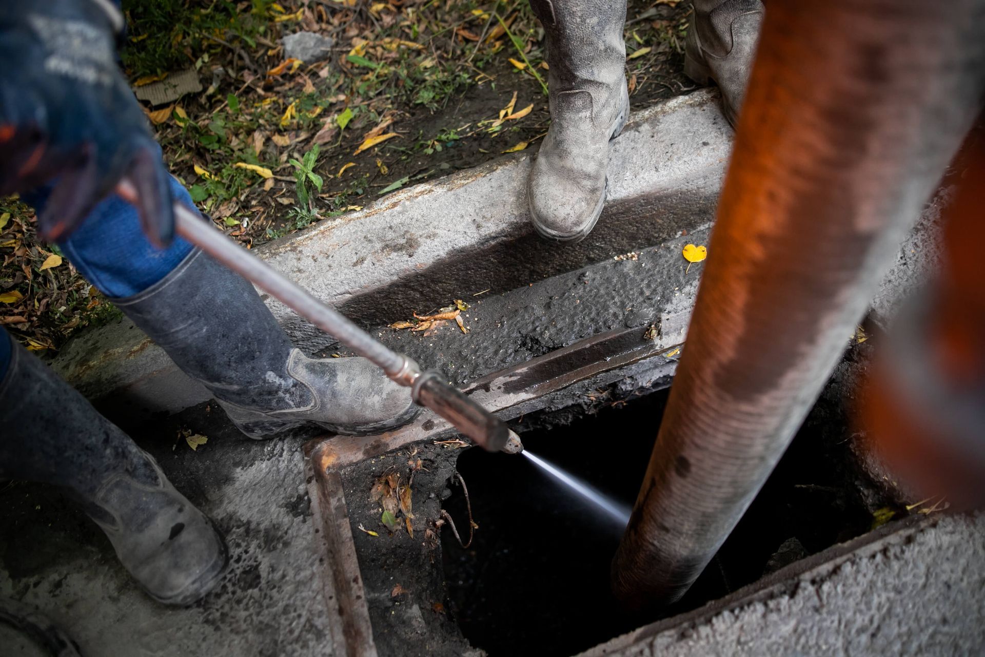 Workers cleaning a sewer line, spraying water into an open manhole.