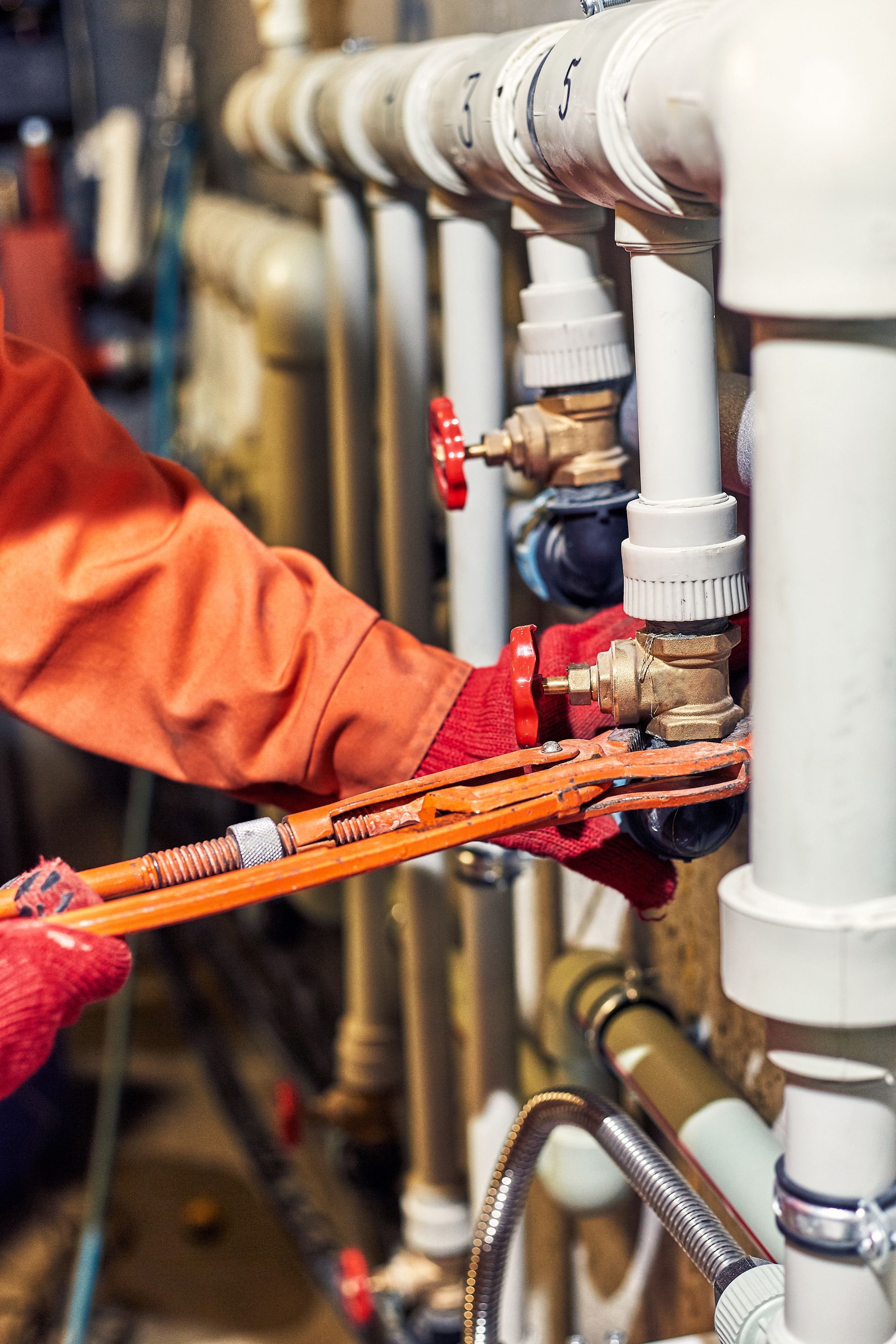 Person in red gloves uses a wrench on pipes in an industrial setting.