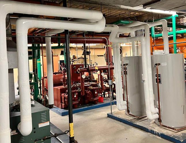 Pipes and machinery in an industrial setting. White insulated pipes, green and orange pipes, and large red machine visible.