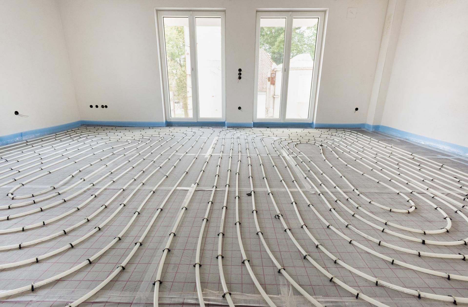 White pipes arranged on a floor, likely for radiant heating, in a room with white walls and windows.
