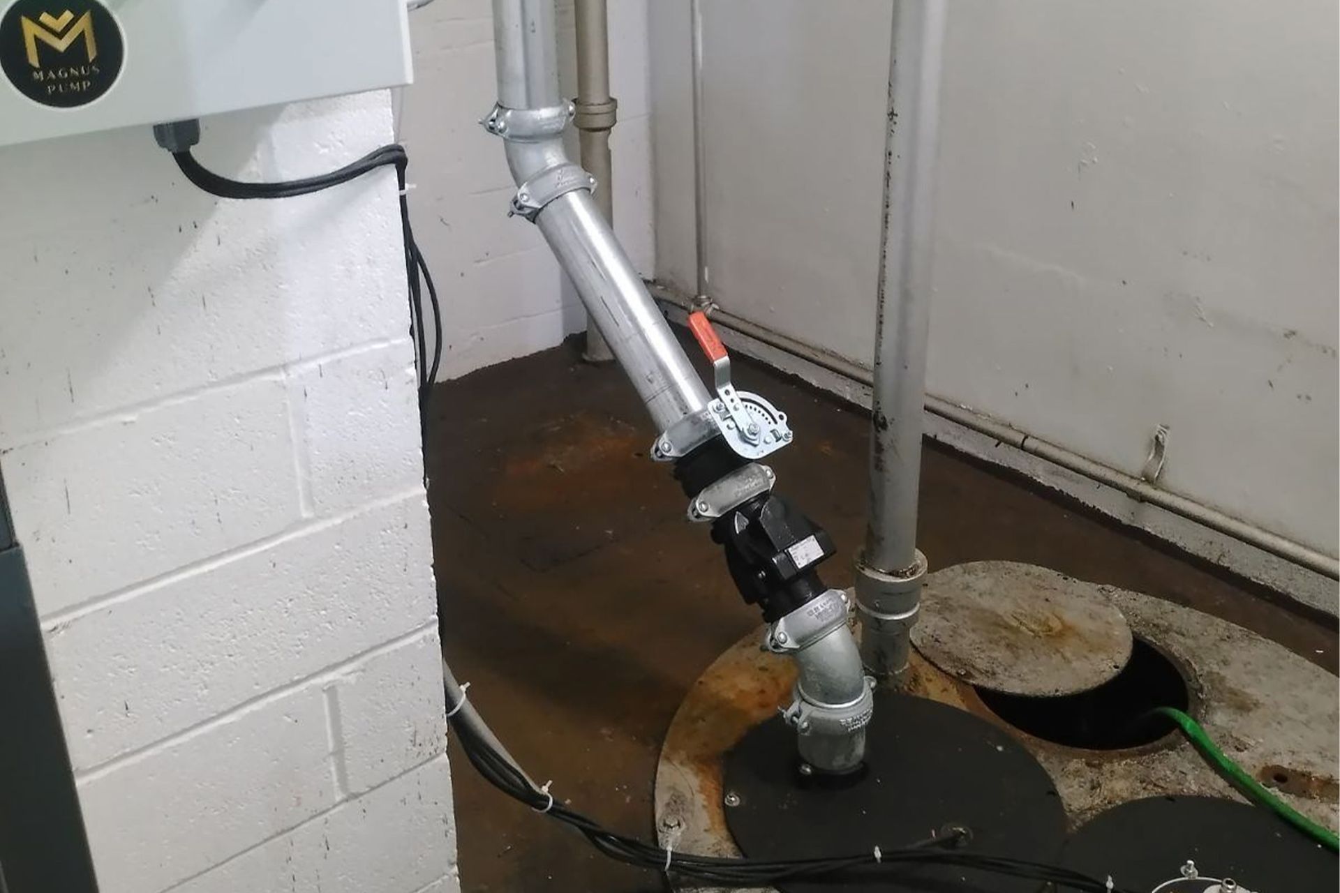 Sump pump with angled discharge pipe in a basement setting near a brick wall.