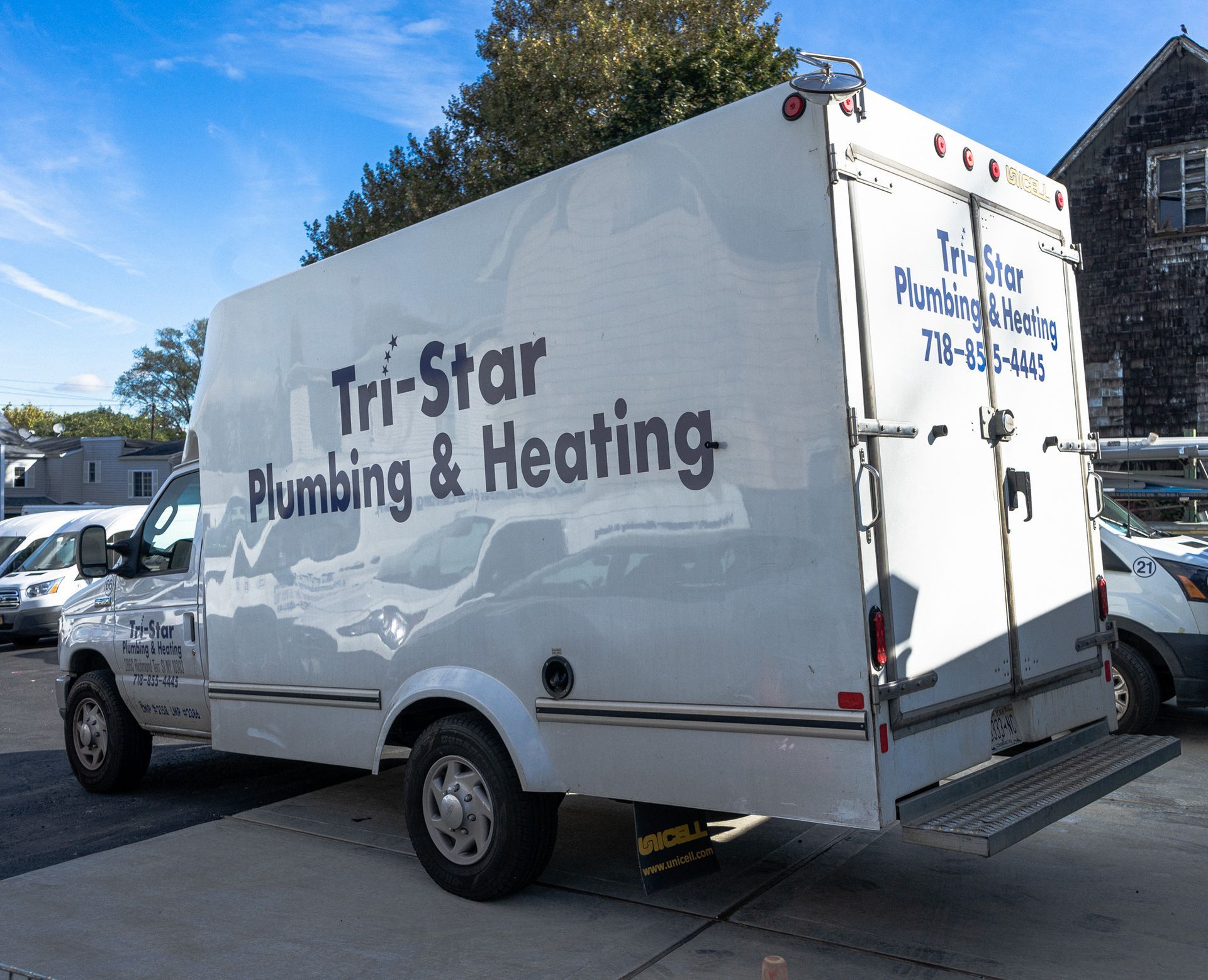 White Tri-Star Plumbing & Heating truck parked outside, text on side, blue sky.