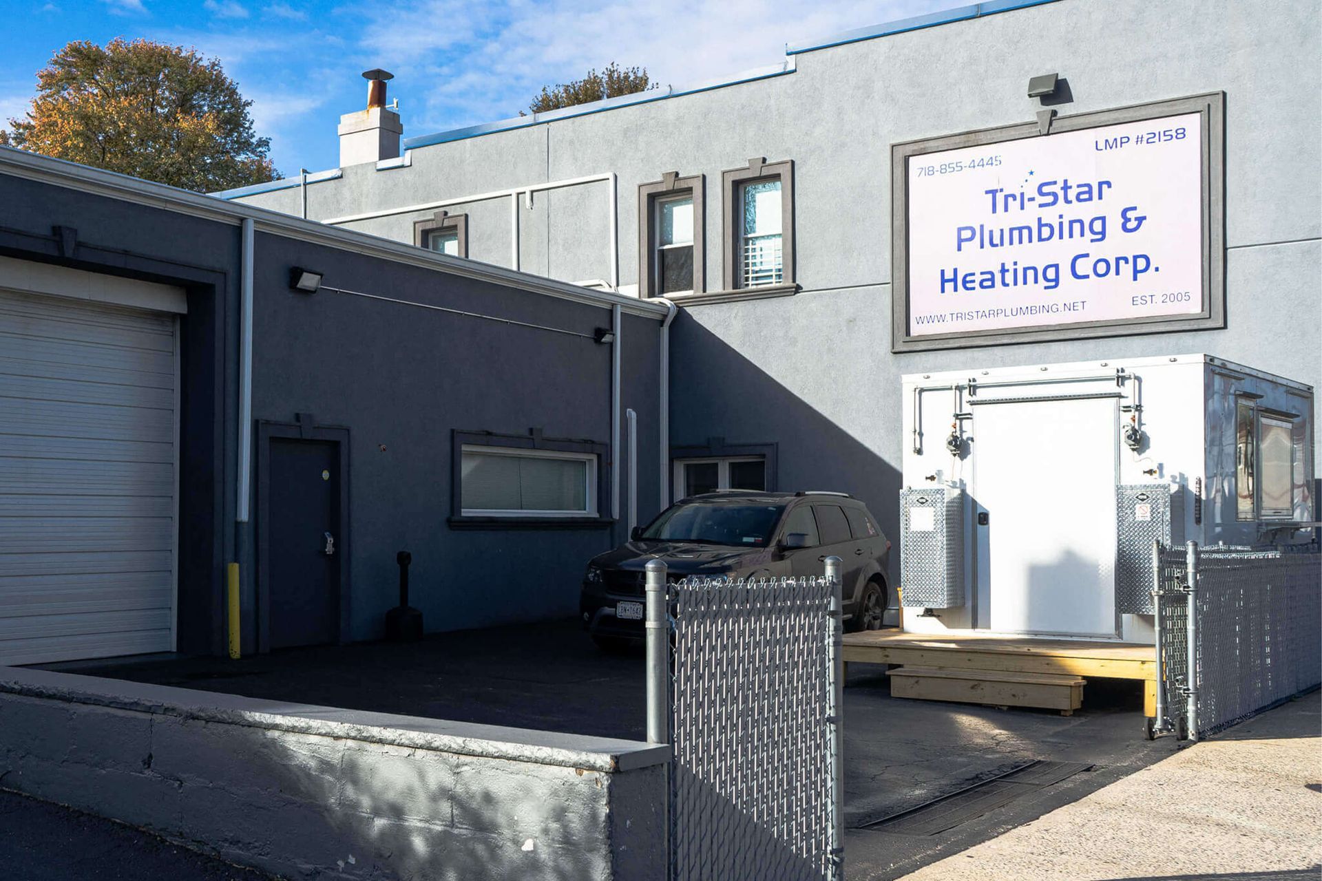 Exterior of Tri-Star Plumbing & Heating Corp. building. Gray exterior, black car parked, sign visible.