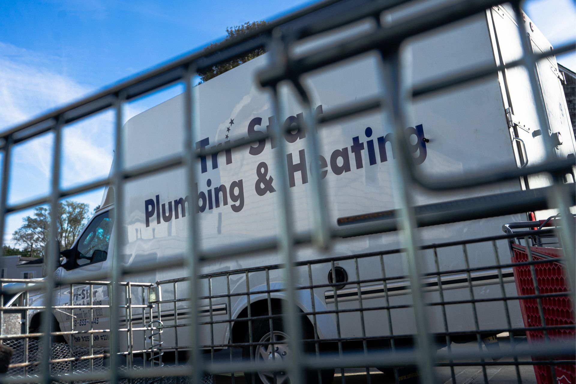 White plumbing and heating van behind a gray metal fence, lettering visible: 